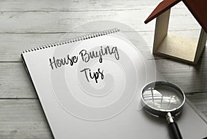 Selective focus of magnifying glass,wooden house and notebook written with House Buying Tips on wooden background photo