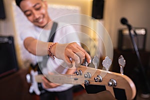 selective focus of a male bassist& x27;s hand tuning an electric guitar bass string before playing