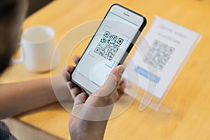 Selective focus of man\'s hand scanning QR code through mobile phone at cafe table