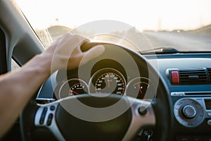 Selective focus man`s hand on steering wheel, driving a car at sunset. Travel background