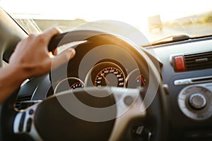 Selective focus man`s hand on steering wheel, driving a car at sunset. Travel background