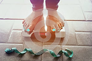 Selective focus of measure tape which woman feet look Lose weight concept  on a scale measuring kilograms on floor background