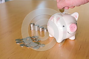 Selective focus of Men hand putting coin to piggy bank with stack of coin on wooden desk fill with natural light background.