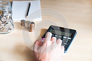 Selective focus at men hand using calculator with increase stack of money and glass jar on wooden desk. Personal financial saving