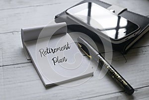 Selective focus of mobile phone,notebook,pen and paper written with Retirement Plan on white wooden background