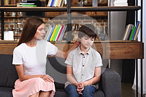 selective focus of mother cheering up depressed little son on sofa