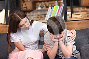 selective focus of mother cheering up depressed little son on sofa