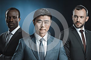 selective focus of multicultural group of businessmen in suits looking at asian colleague