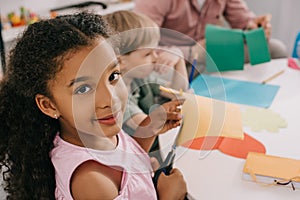 selective focus of multiethnic preschoolers cutting colorful papers with scissors