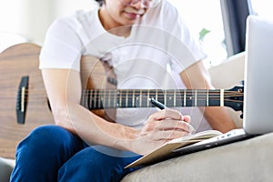 Selective focus of musician's hand composing music with acoustic guitar in living room