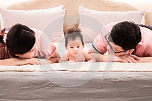 Selective focus of newborn baby laying down on bed, father and mother looking at daughter with love and tender, parents spending