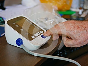 Selective focus of an old man`s hand placed next to the monitor checking his blood pressure at home by himself