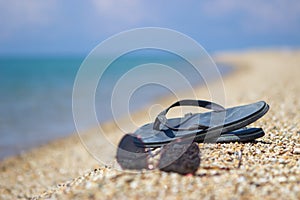 Selective focus on old slippers. Next are sunglasses. They are located on the yellow sand on the beach and it is a beautiful sunny