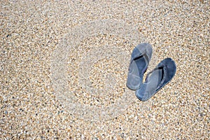 Selective focus on old slippers. The slippers are on the yellow sand on the beach and it is a beautiful sunny day. Copy space