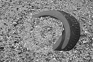 Selective focus of an old tyre covered with mud and shells by the beach. Photo in black and white