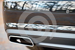 Selective focus on parking sensor exhaust pipe bumper at rear of black luxurious car bumper close up on light blurred background