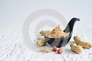 Selective focus on peanut butter in a black ceramic cup placed on surface of white wooden plank