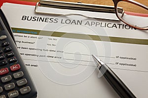 selective focus pen,Business loan application form,glasses ,calculator,red paper clip on wood background.