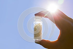 Selective focus on person hand holding glass jar full of small white round homeopathy pills.