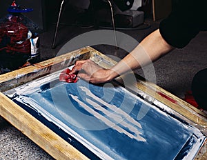 Selective focus photo of male hand with red cloth, cleaning print frame. serigraphy production. printing images on t-shirts by