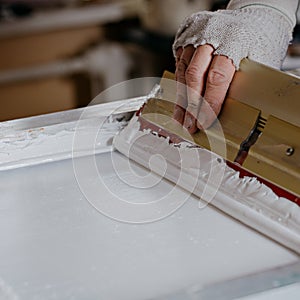 Selective focus photo of male hand with squeegee. serigraphy production. printing images on t-shirts by silkscreen method in a