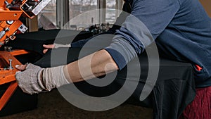 Selective focus photo of male hands with t-shirt on wooden shelve on the print screening apparatus. serigraphy production.