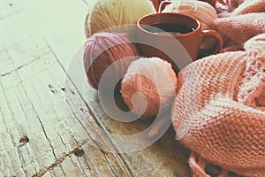 Selective focus photo of pink cozy knitted scarf with to cup of coffee and wool yarn balls on a wooden table