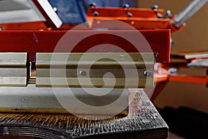 Selective focus photo of a squeegee on wooden shelve of the print screening apparatus. serigraphy production