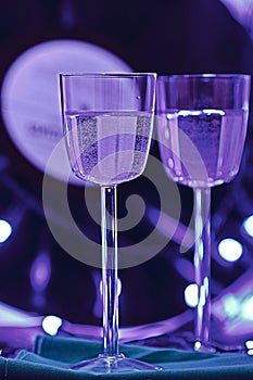 Selective focus photo of two glasses of champagne on the background of a vinyl record, surrounded by bright club illumination