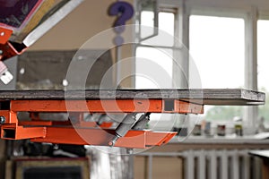 Selective focus photo of a wooden shelve for placing t-shirts on the print screening apparatus. serigraphy production. printing