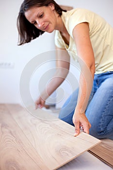 Selective focus photo of a young woman installing laminate flooring. Home improvement and renovation concept