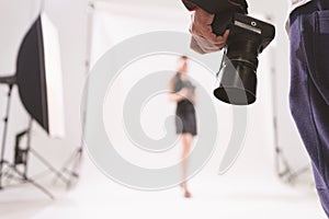 Selective focus of photographer holding camera in a photoshoot with blurry model at the background, behind the scene of model