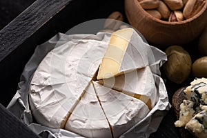 Selective focus of pieces of camembert with dorblu, dried olives and pistachios on tray.