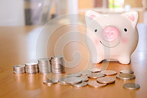 Selective focus piggy bank coin with stack of coin on wooden desk fill with natural light background. Saving money and financial,