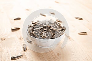 Selective focus pile of sunflower seeds in the white bowl on the wooden table