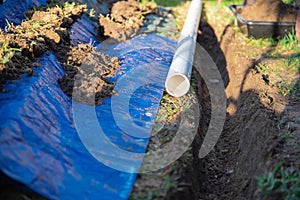 Selective focus plastic sewage pipes PVC, blue tarp with dirt, black mixing tub, pipe ready to laying, buried in ground trench,
