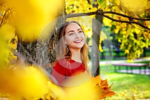 Selective focus. Portrait of an attractive young blonde in a red knitted dress with a bouquet of fallen yellow leaves, smiling in