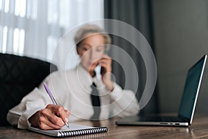 Selective focus portrait of busy middle-aged business woman multitasking in office, working online with laptop, talking