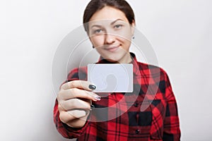 Selective focus. Portrait of female businesswoman in checked red shirt holding a parchment business card with copy space for your