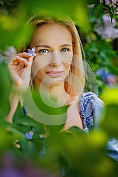 Selective focus. Portrait of a young beautiful blonde with blue eyes, posing among the blooming lilacs. Street fashion photo of a
