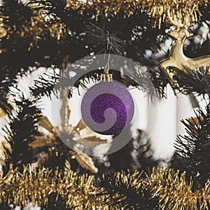 Selective focus of a purple glitter shatterproof ball on a Christmas tree with Christmas decorations