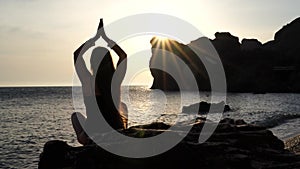 Selective focus. Rear view of a young beautiful caucasian woman practicing yoga on the beach at sunset by the sea. Yoga