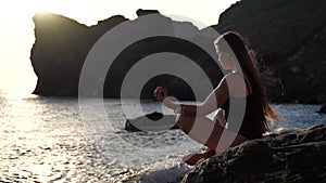 Selective focus. Rear view of a young beautiful caucasian woman practicing yoga on the beach at sunset by the sea. Yoga