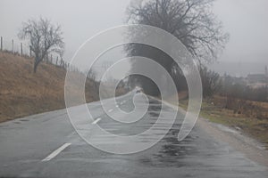 Selective focus of road and trees during autumnal rain with grey sky on background