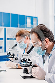 selective focus of scientists in medical masks and goggles looking through microscopes on regents