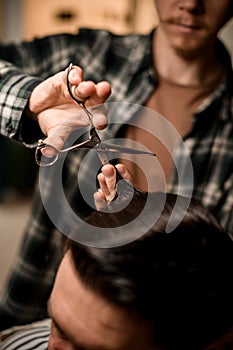 selective focus on scissors in the hands of barber who skillfully cuts hair of client in barbershop.