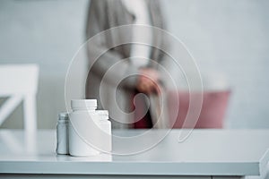 selective focus of senior woman with walking stick standing in room with medicines on tabletop at home