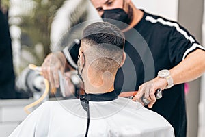 Selective focus on the shaved nape of a man with mask in a barbershop