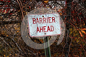 Selective focus shot of a barrier ahead sign leaned against a metal fence