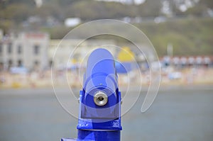 Selective focus shot of a blue telescope with a blurred lake and buildings in the background